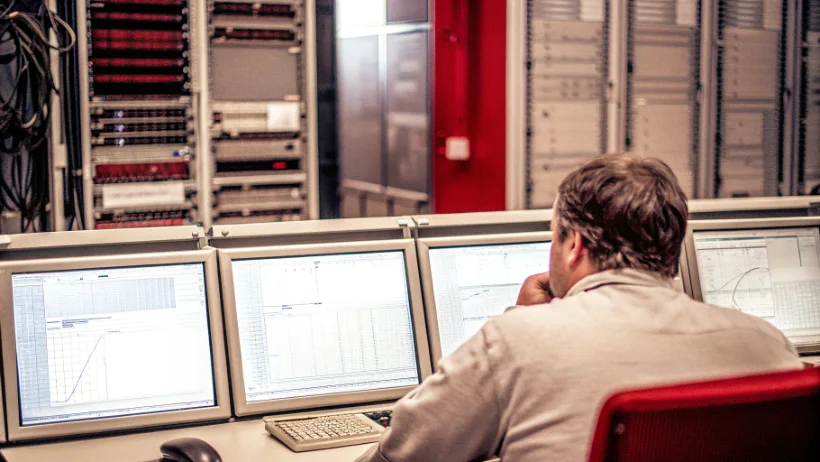 Network engineer monitoring multiple screens displaying data center performance metrics